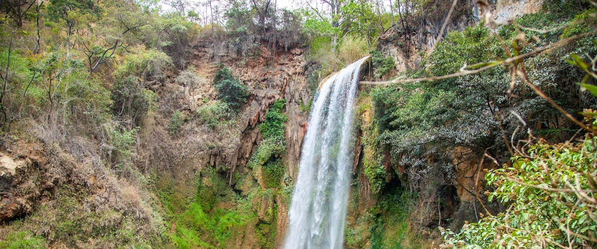A waterfall cascading into a turquoise pool surrounded by rocky cliffs and greenery.
