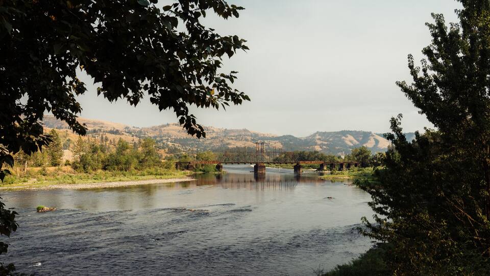 A river with a bridge, surrounded by hills and trees.