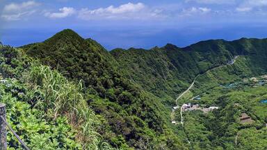 A mountainous landscape with dense forests, a winding road, and scattered buildings.