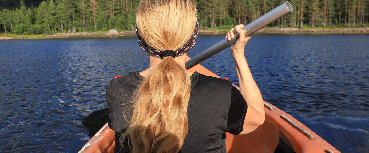 A person in a canoe on a lake with a forest and hills in the background.