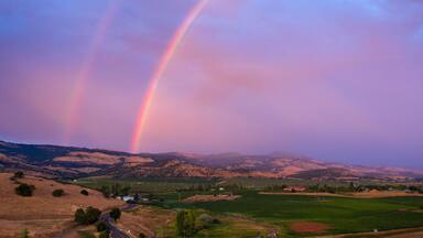 A landscape with rolling hills, a winding road, and a rainbow.