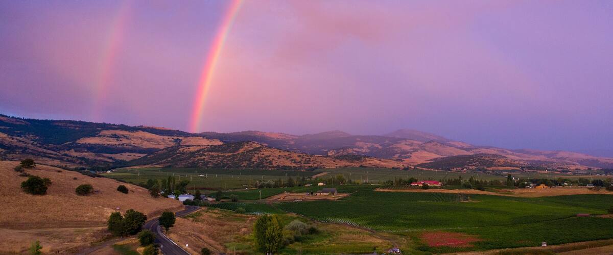 A landscape with rolling hills, a winding road, and a rainbow.