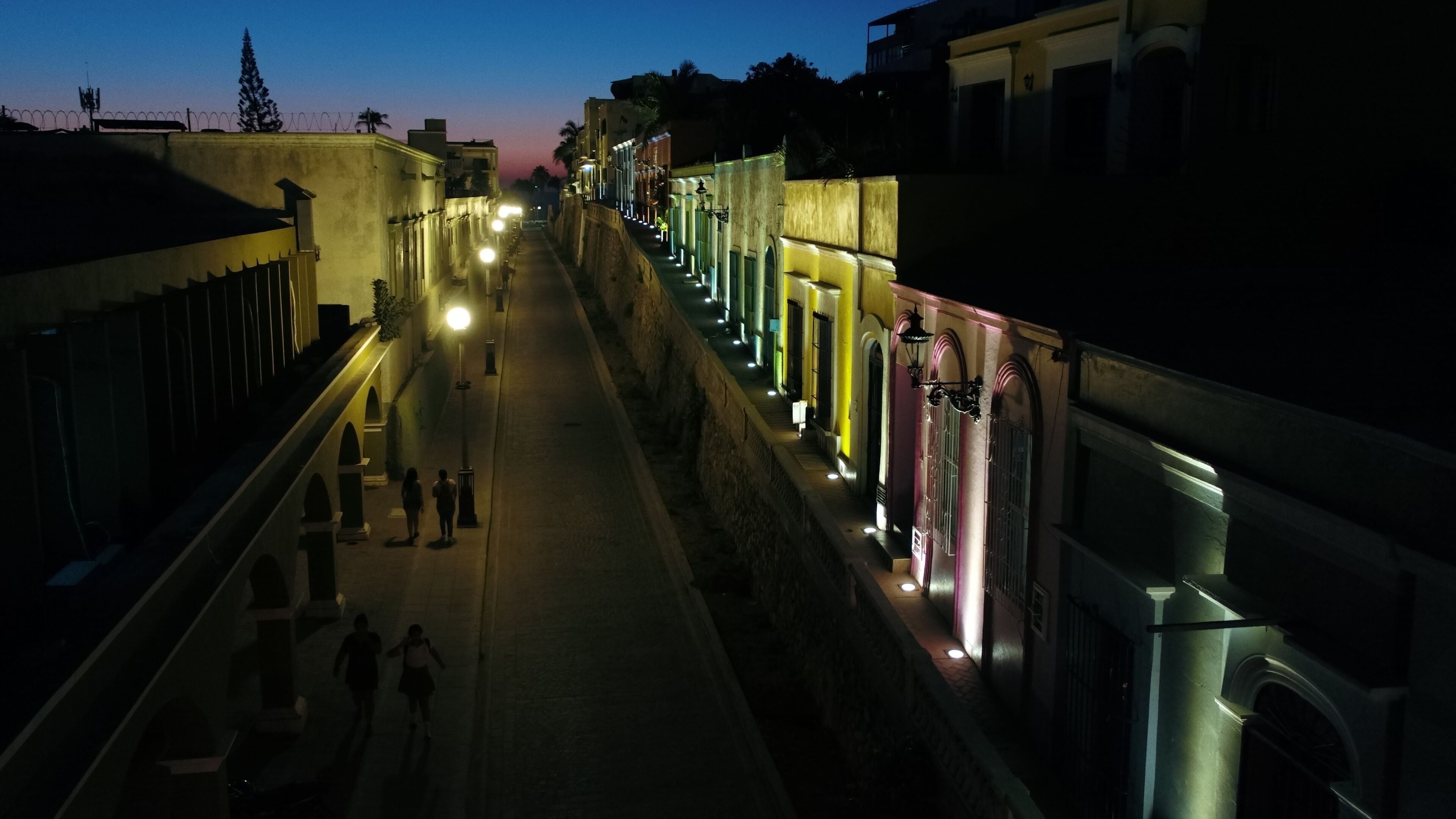 Una calle tenuemente iluminada con edificios a ambos lados, que presentan ventanas de arco y un pasaje central.