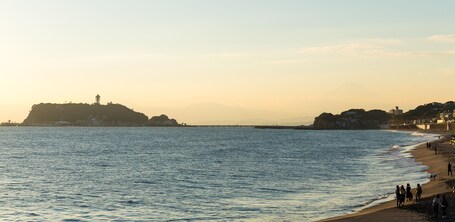 Eine Küstenlandschaft mit Strand, einer Mole und einem Hügel mit einem Leuchtturm.