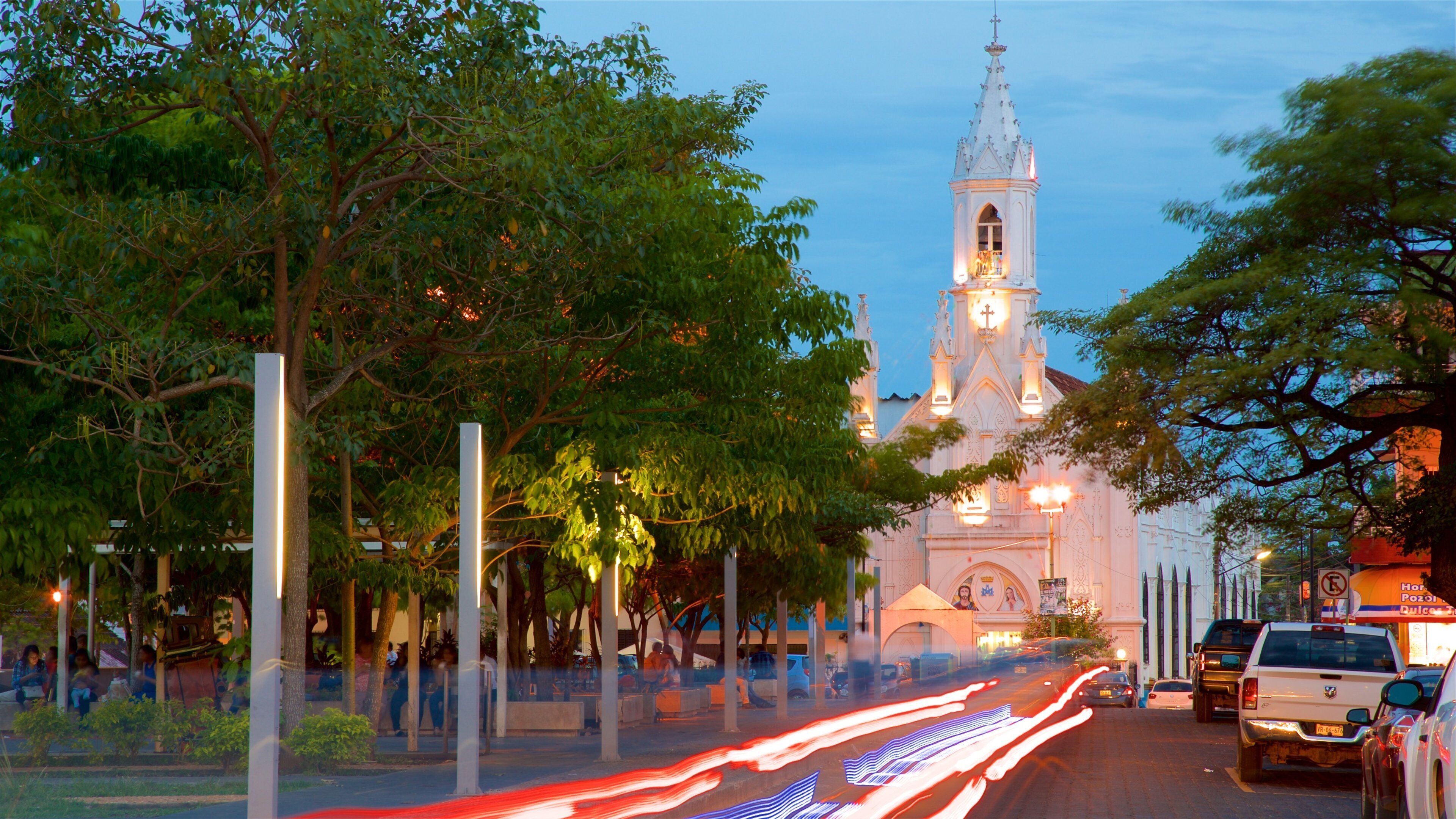 A church with a tall steeple and a clock tower, surrounded by trees and streetlights.