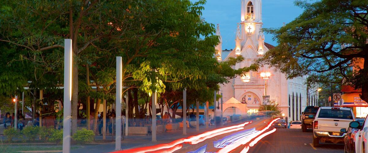 A church with a tall steeple and a clock tower, surrounded by trees and streetlights.