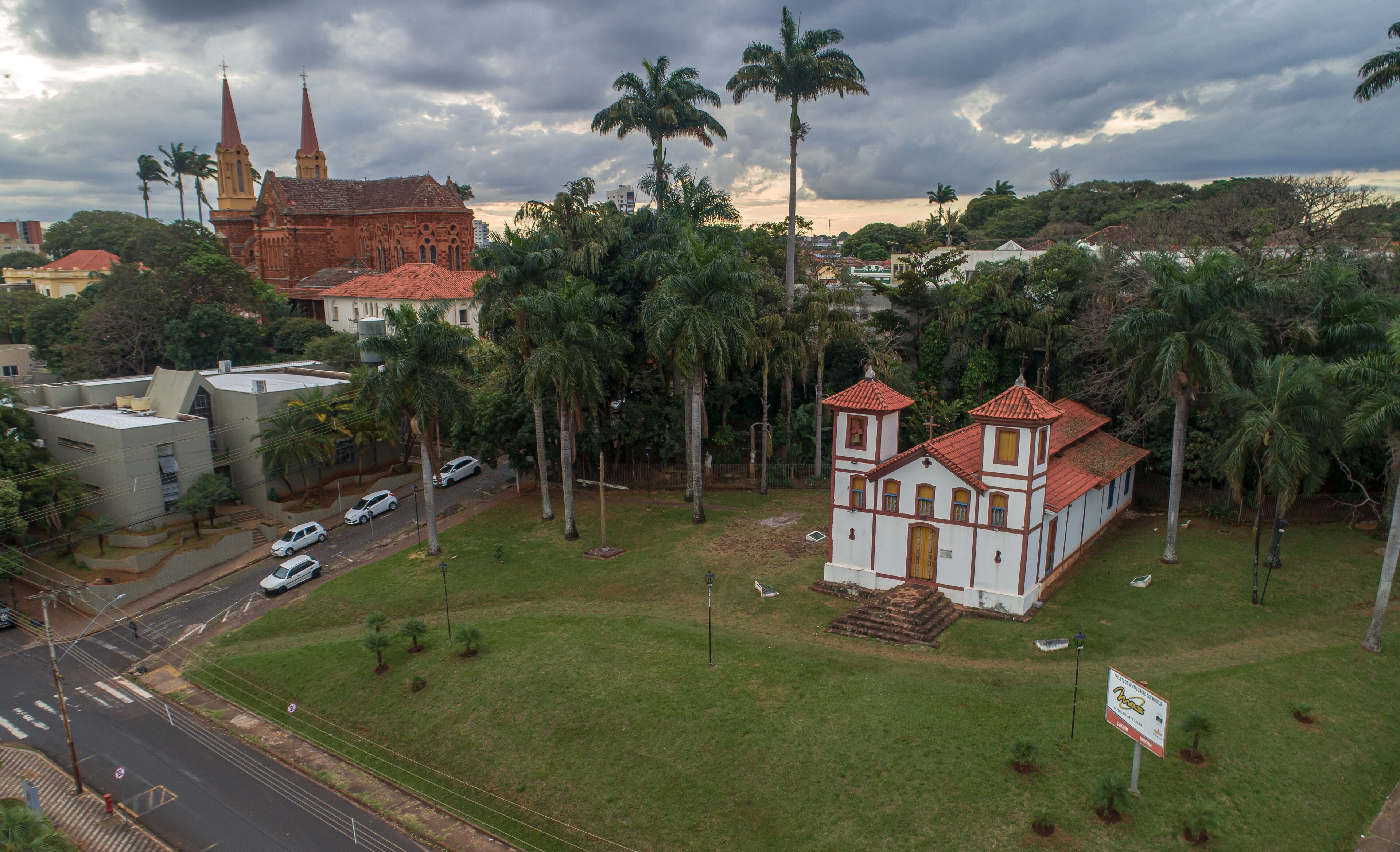 A church with a red roof, surrounded by palm trees and a grassy area.