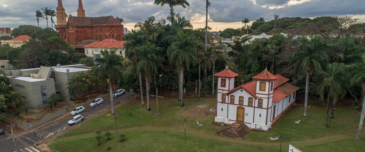 A church with a red roof, surrounded by palm trees and a grassy area.