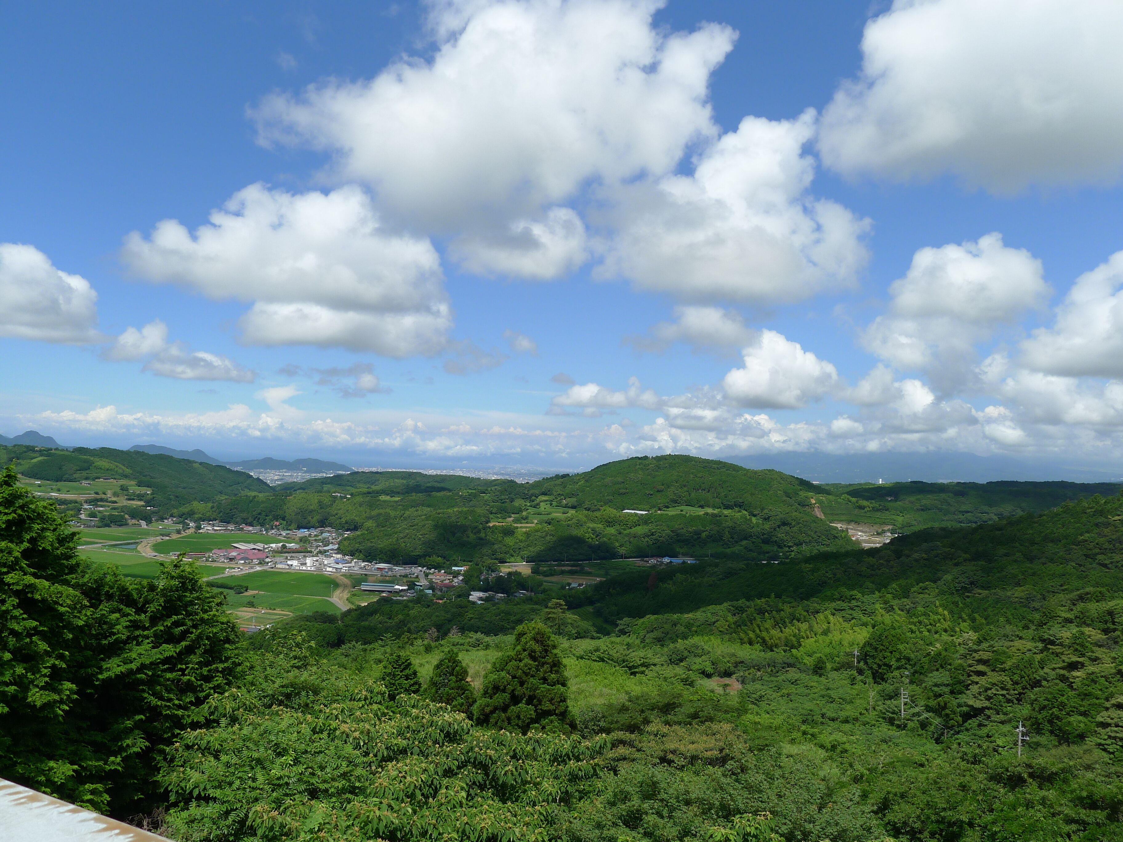 A lush green valley with rolling hills, a small town, and a clear blue sky with scattered clouds.