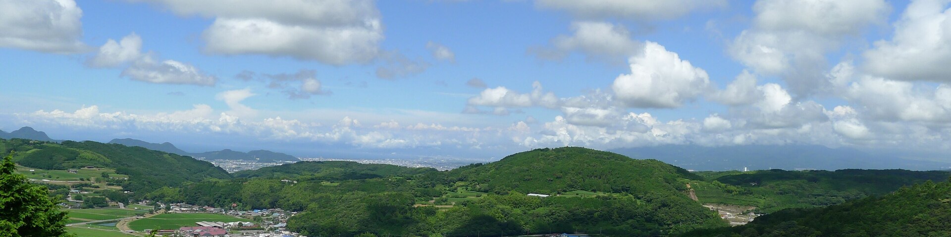 A lush green valley with rolling hills, a small town, and a clear blue sky with scattered clouds.