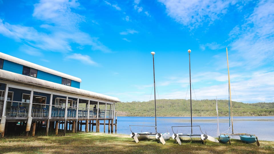 A lakeside building with a dock, sailboats, and a clear blue sky.