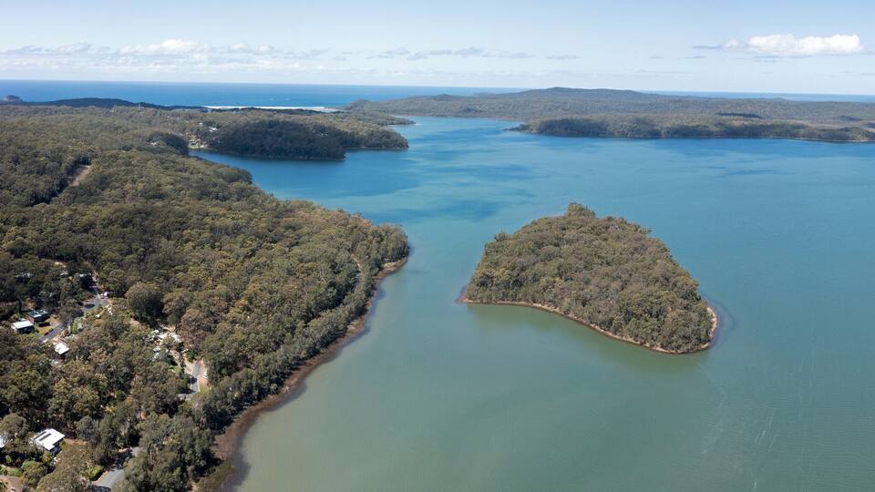 A coastal landscape with a large body of water surrounded by forested hills.