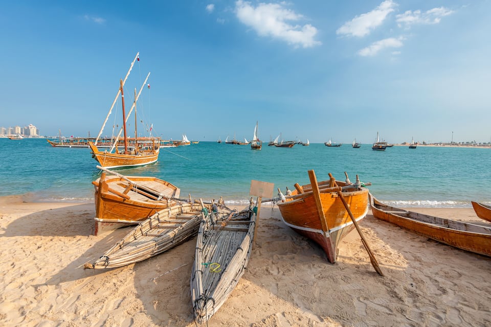 Ein sandiger Strand mit mehreren Holzbooten und einem klaren, blauen Meer.