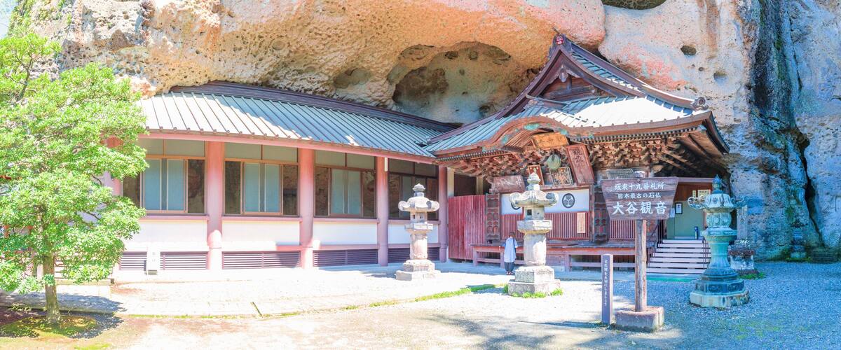 A traditional Japanese building with a tiled roof, surrounded by rocky cliffs and greenery.
