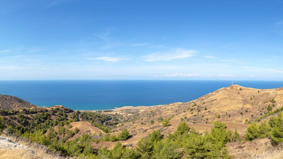A mountainous landscape with a clear view of the sea and a lighthouse on a hill.