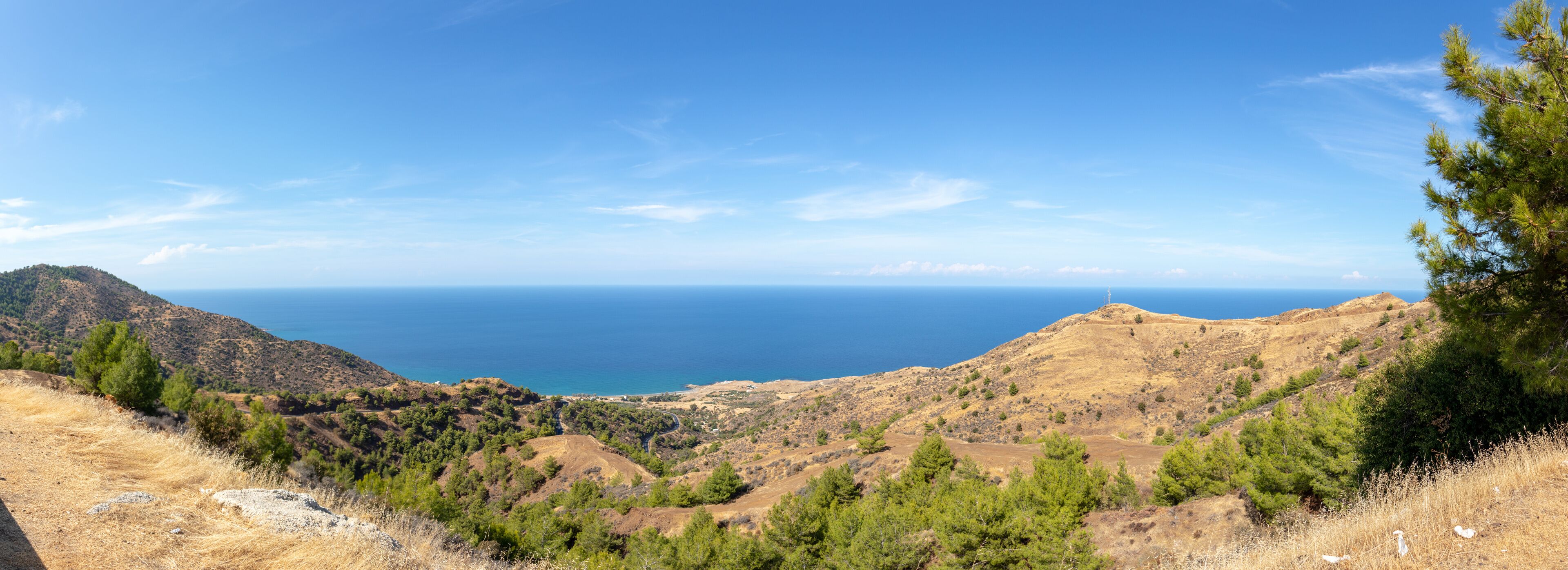 A mountainous landscape with a clear view of the sea and a lighthouse on a hill.