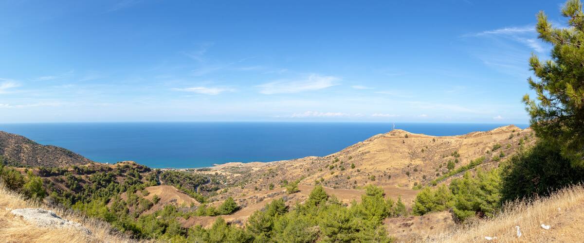 A mountainous landscape with a clear view of the sea and a lighthouse on a hill.