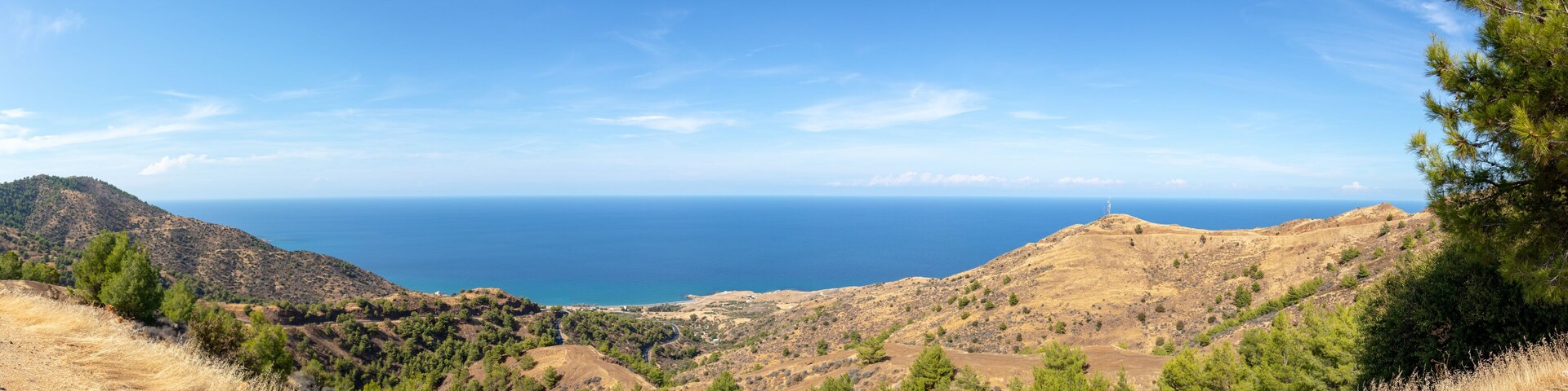 A mountainous landscape with a clear view of the sea and a lighthouse on a hill.
