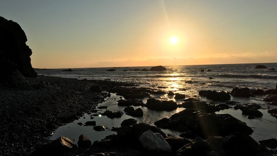 A rocky beach at sunset with the sun low on the horizon.