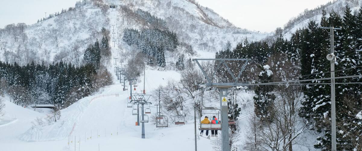 A snow-covered ski lift with passengers, surrounded by snow-laden trees and mountains.