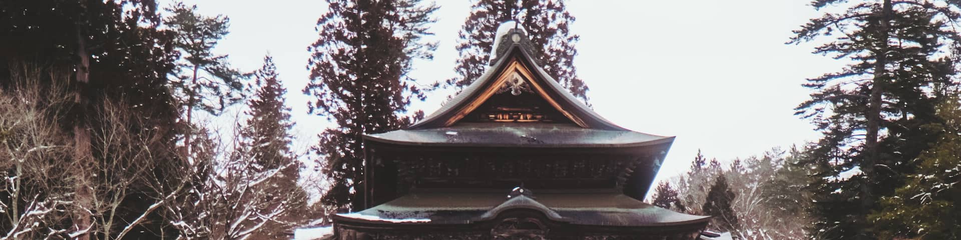 View of a traditional Japanese temple perched atop rocky cliffs, surrounded by snow-dusted trees and a serene, wintry landscape, Yanaizu, Fukushima, Japan.