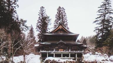 View of a traditional Japanese temple perched atop rocky cliffs, surrounded by snow-dusted trees and a serene, wintry landscape, Yanaizu, Fukushima, Japan.