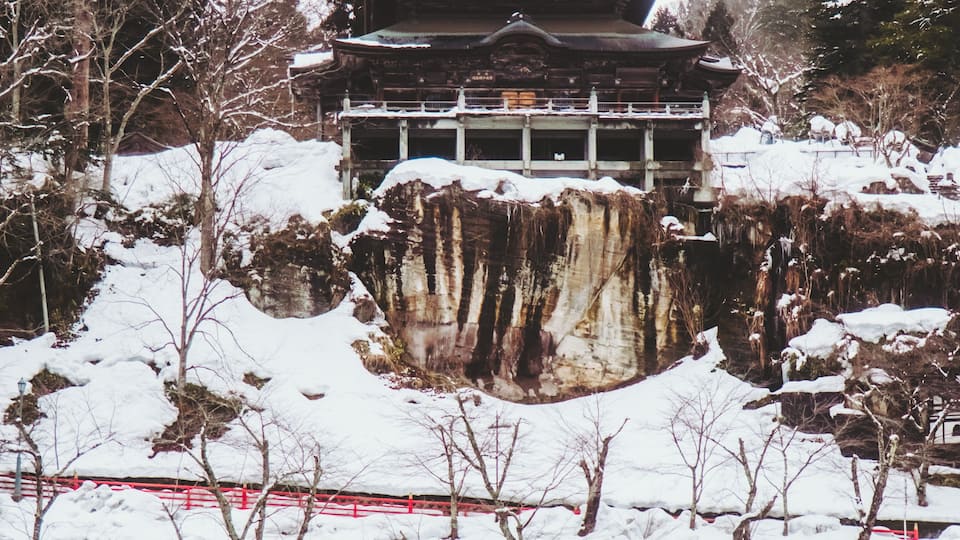 A traditional Japanese building with a snow-covered landscape and a bridge.