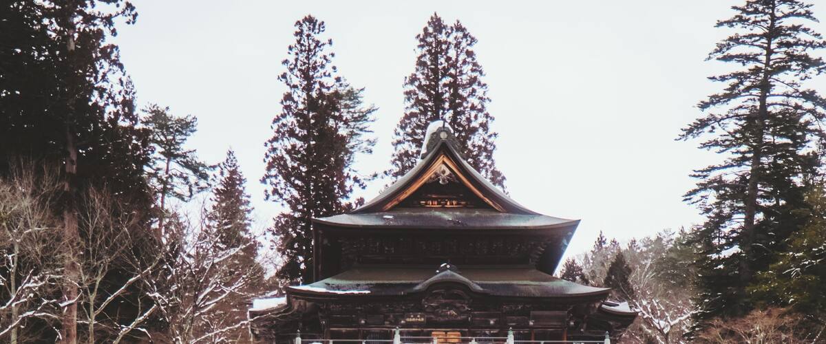 A traditional Japanese building with a snow-covered landscape and a bridge.