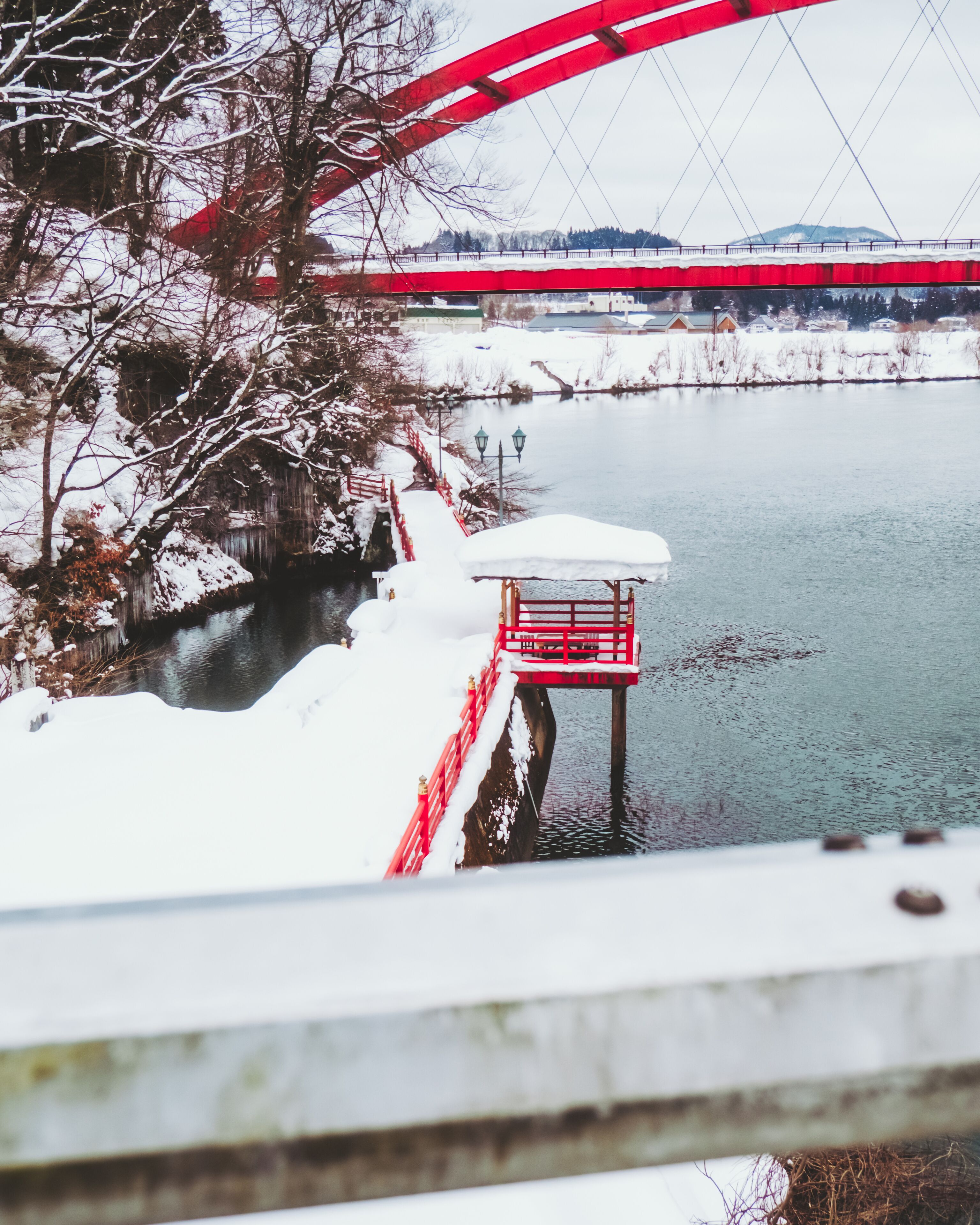View of a vibrant red bridge arches gracefully over the tranquil river, a snowy scene contrasting with the vivid structure, Yanaizu, Fukushima, Japan.