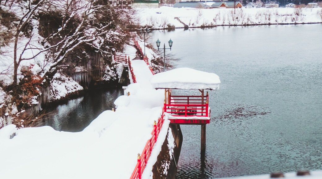 View of a vibrant red bridge arches gracefully over the tranquil river, a snowy scene contrasting with the vivid structure, Yanaizu, Fukushima, Japan.