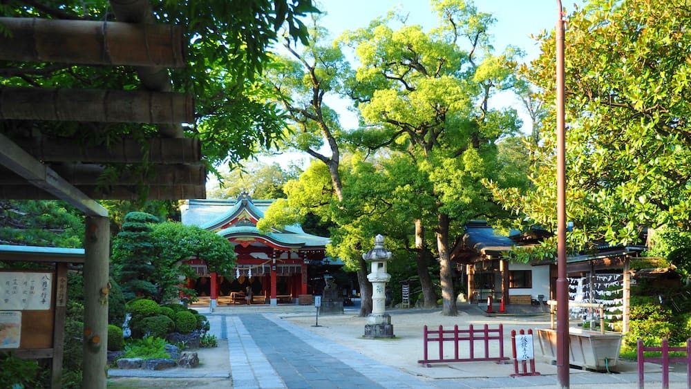 Ein traditioneller japanischer Tempel mit einem steinbelagten Weg, der zum Eingang führt, umgeben von üppigem Grün und blauem Himmel.