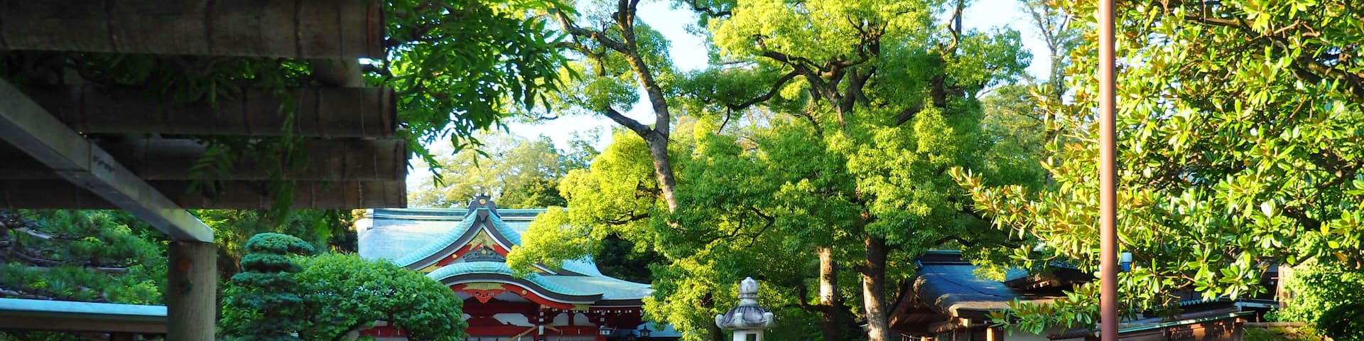 A traditional Japanese temple with a stone pathway leading to the entrance, surrounded by lush greenery and a clear blue sky.