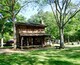 A rustic log cabin surrounded by lush green trees in a park.