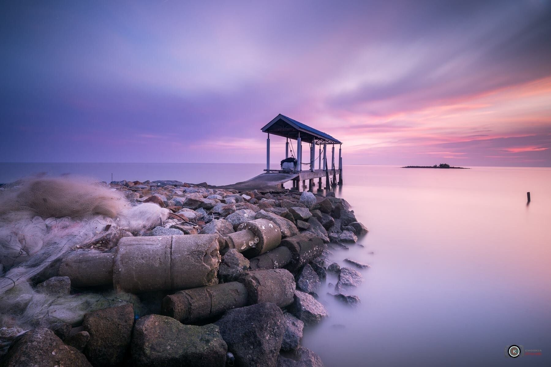 A pier extending into calm waters with a sunset sky.