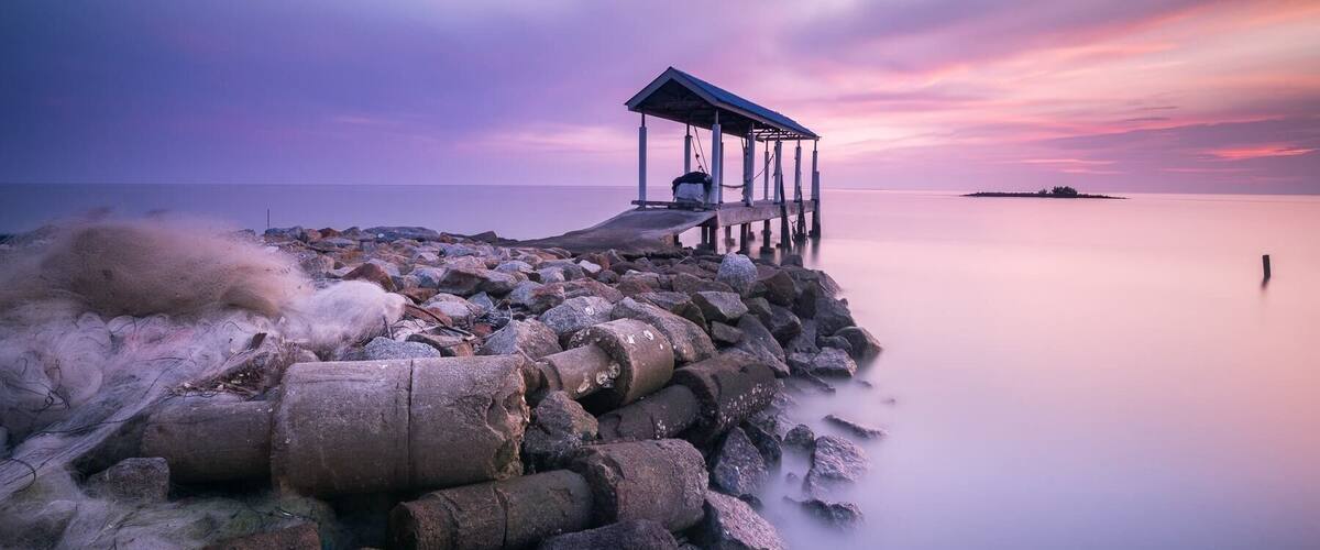 A pier extending into calm waters with a sunset sky.