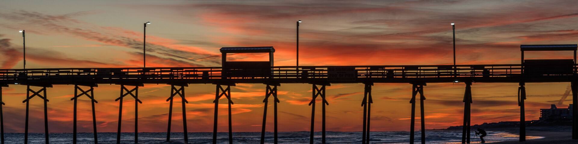 Colorful Sunset at ocean coast with silhouette of pier and photographer