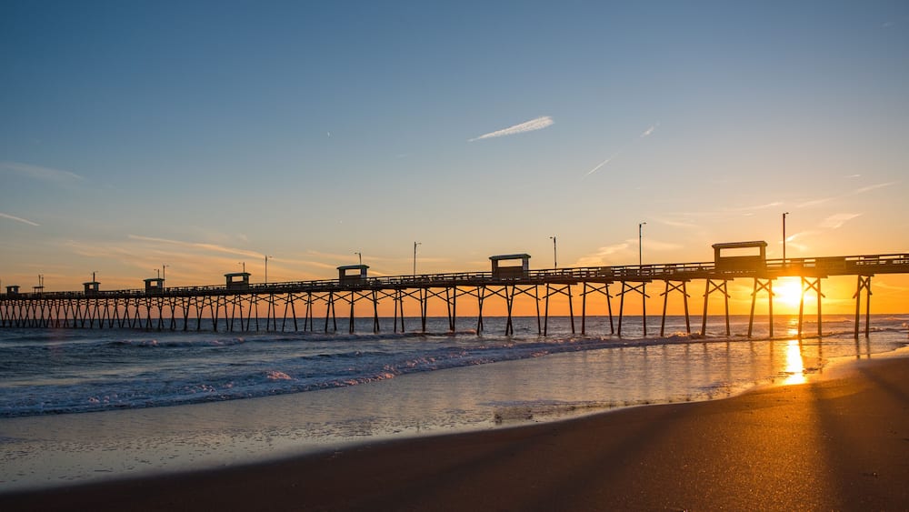 Colorful Sunset at ocean coast with silhouette of pier and photographer