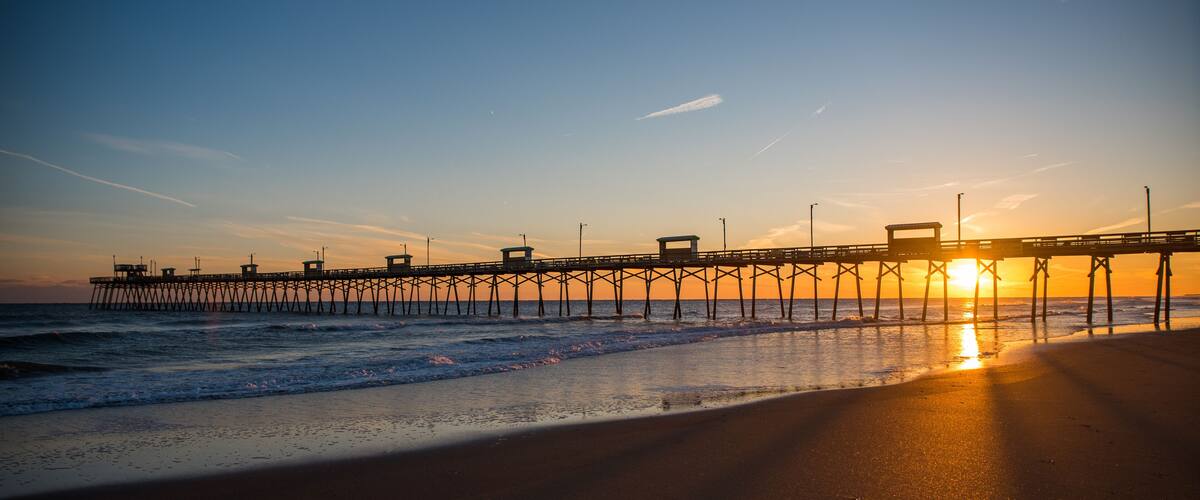 Colorful Sunset at ocean coast with silhouette of pier and photographer