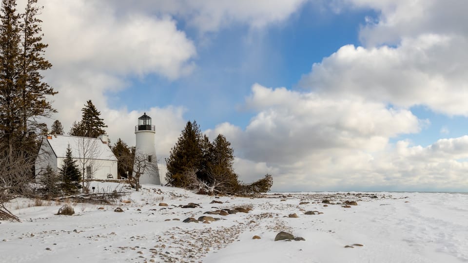 A lighthouse, snow-covered landscape, and a partly cloudy sky.