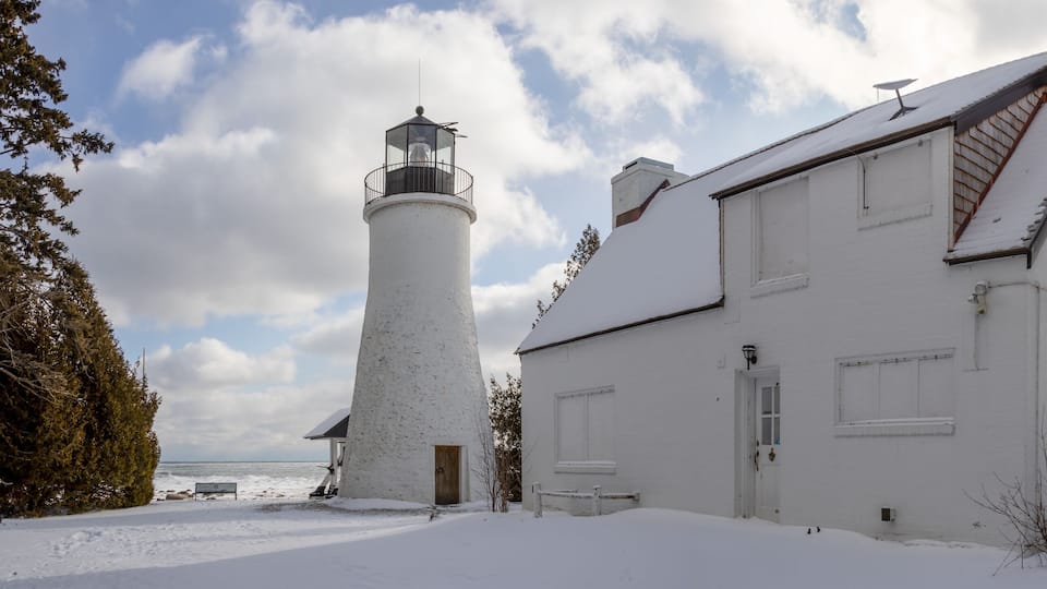 A snow-covered lighthouse and a white building by a body of water.