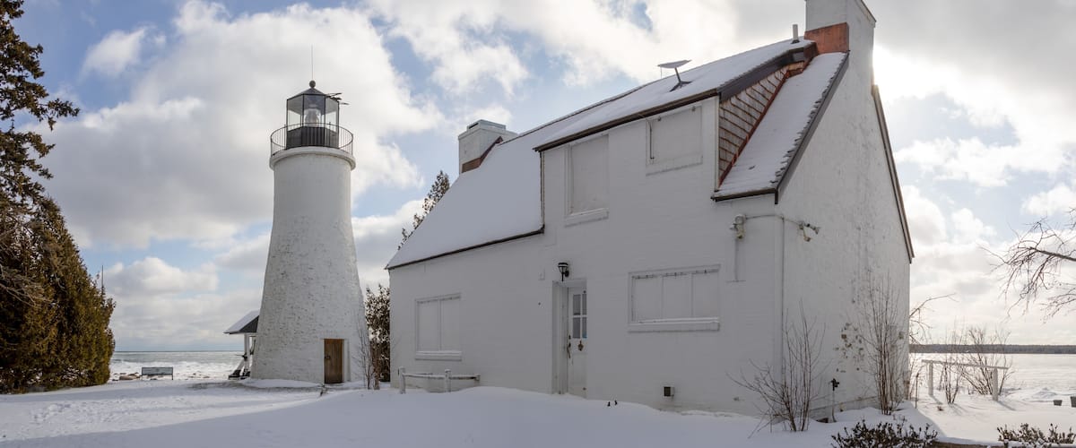 A snow-covered lighthouse and a white building by a body of water.