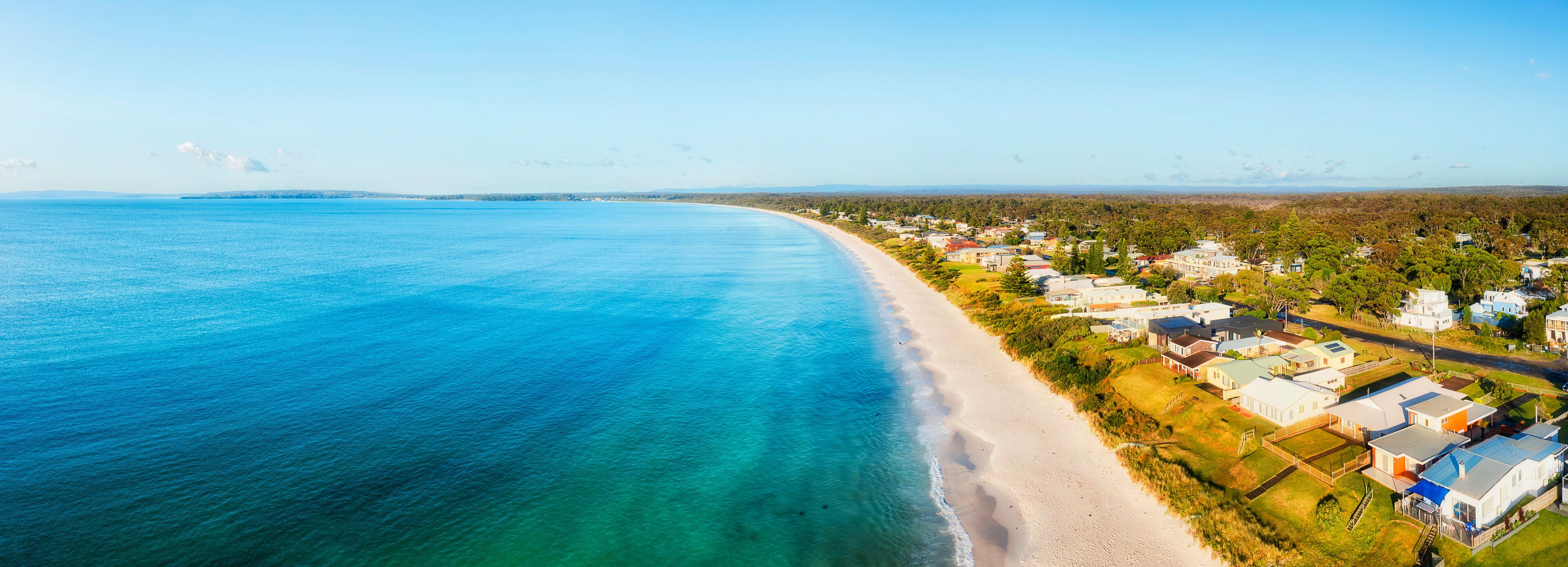 A coastal town with a beach and houses along the shoreline.
