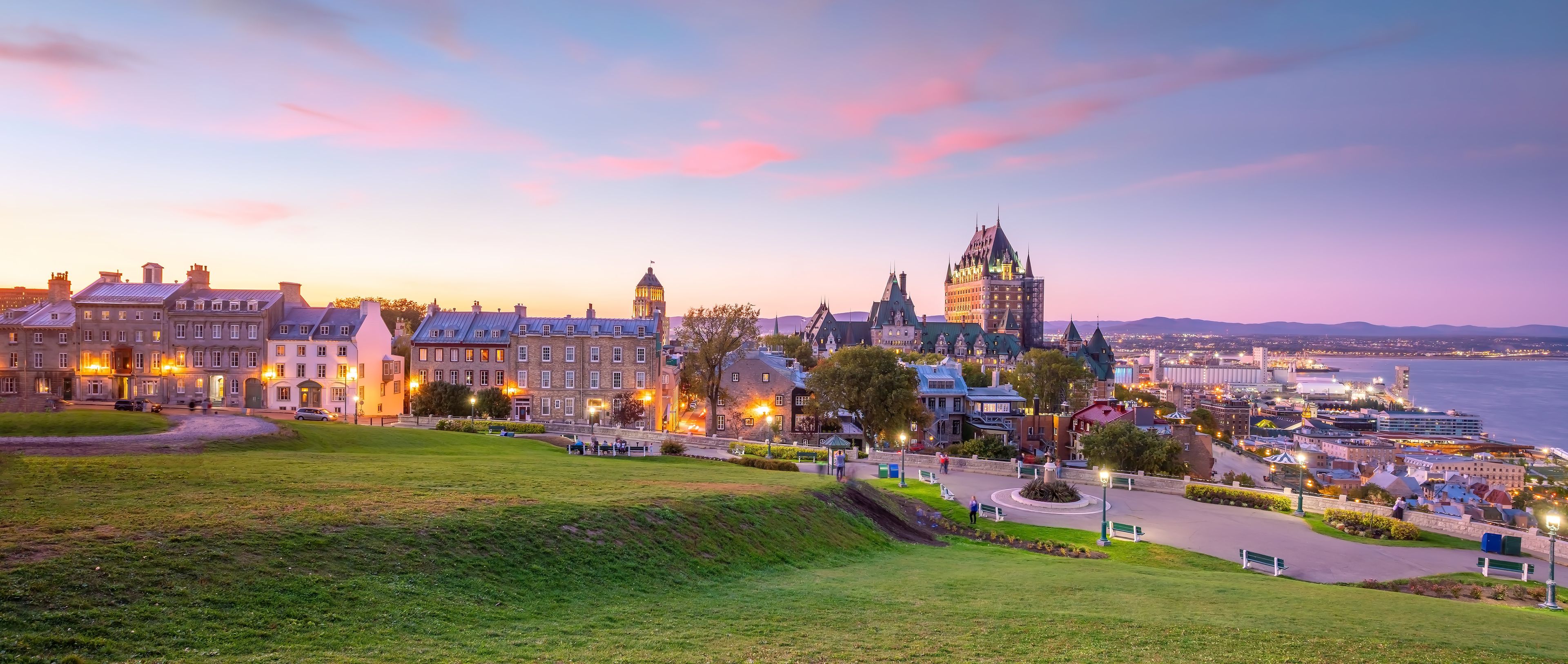 Un paisaje urbano costero al atardecer, con edificios históricos, una destacada torre del reloj y un paseo marítimo.