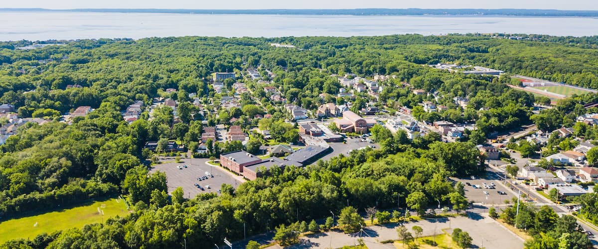 A town with dense green trees, a large body of water in the background, and a mix of residential and commercial buildings.