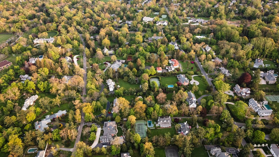 An aerial view of a residential area with houses, trees, and a tennis court.