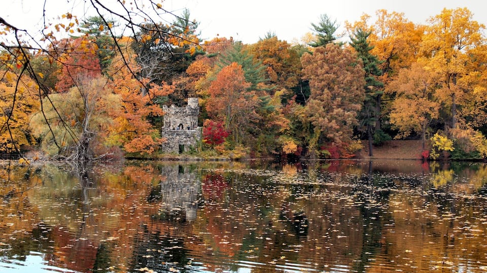A stone tower surrounded by autumn foliage and a reflective lake.