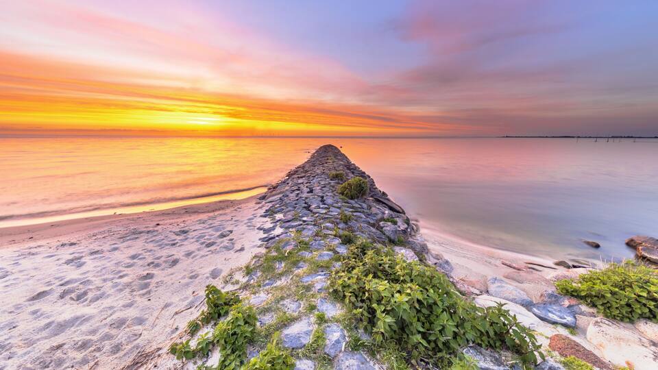 A stone pier extending into calm waters at sunset.
