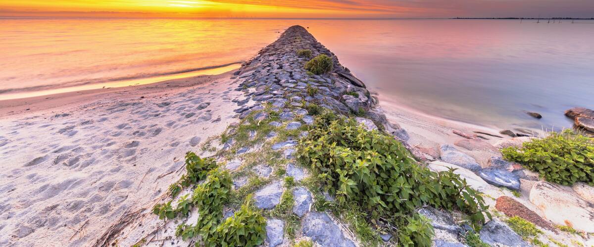 A stone pier extending into calm waters at sunset.