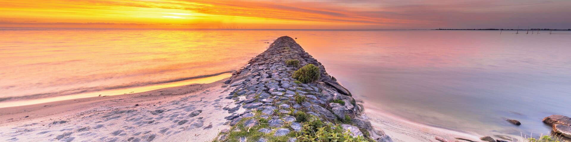 A stone pier extending into calm waters at sunset.