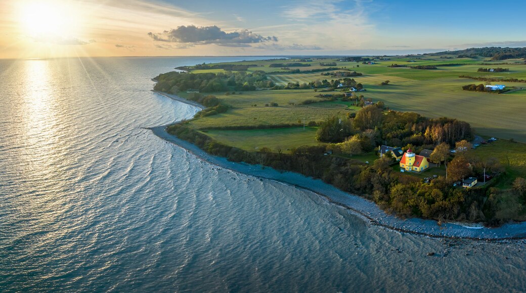 View of Møn lighthouse, distinguished by its striking yellow tower, white gallery, and vibrant red-roofed lantern and pebble beach at Møn’s south-eastern point where the majestic Møns Klint rises.